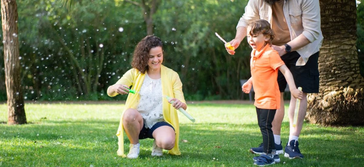 A family enjoys a playful day with bubbles in a sunny park setting.