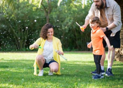 A family enjoys a playful day with bubbles in a sunny park setting.