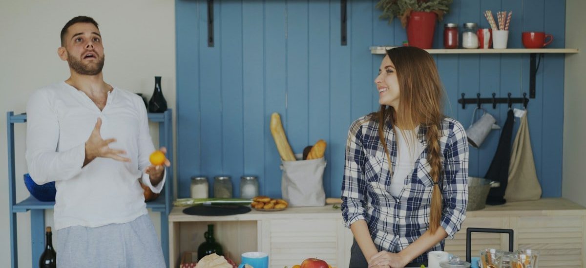 Attractive loving couple having fun in the kitchen. Handsome man juggle with fruits to impress his girlfriend at home