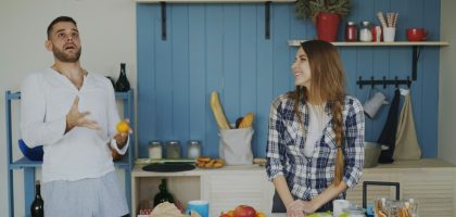 Attractive loving couple having fun in the kitchen. Handsome man juggle with fruits to impress his girlfriend at home