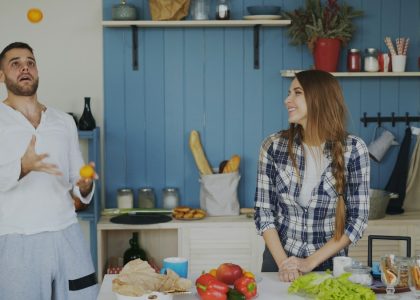 Attractive loving couple having fun in the kitchen. Handsome man juggle with fruits to impress his girlfriend at home