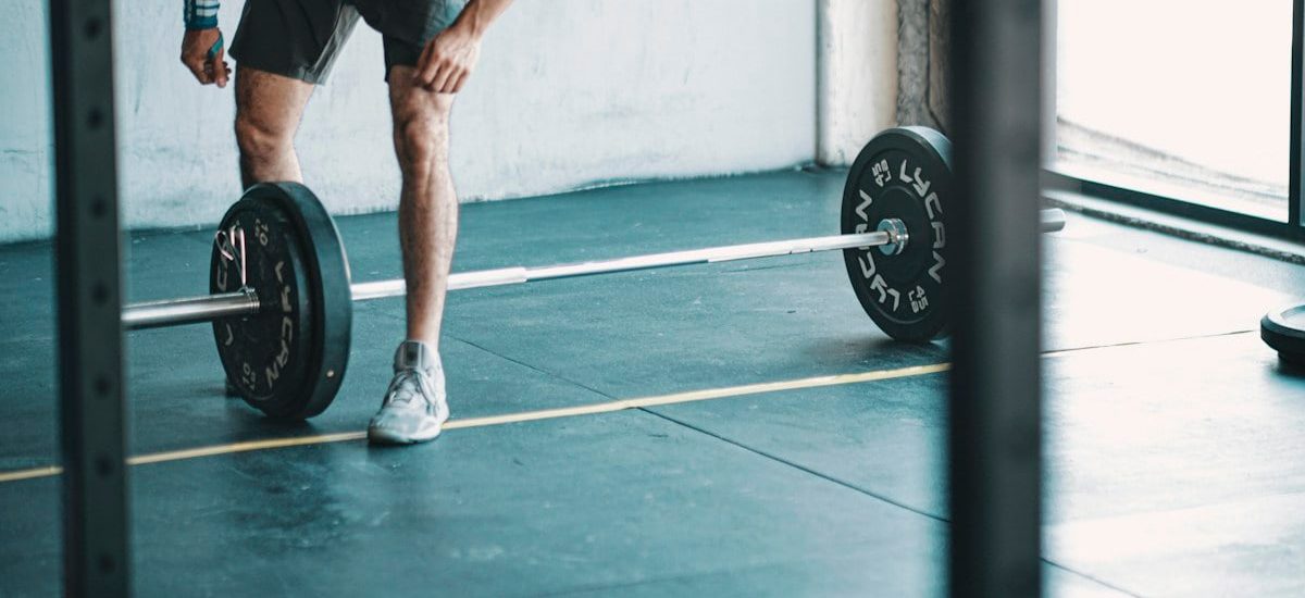 man in black t-shirt and black shorts holding black barbell